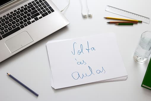 Imagem com notebook e escrita de volta às aulas em cima de mesa com lapis, régua e um copo.